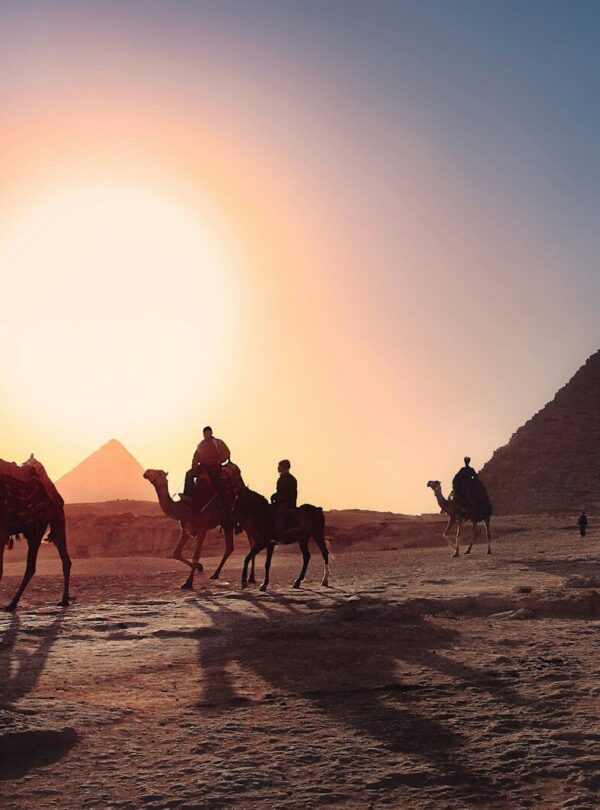 five persons riding camels walking on sand beside Pyramid of Egypt