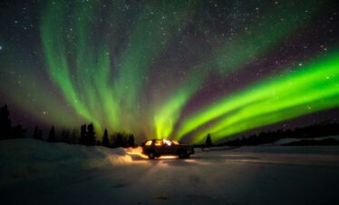 a truck driving down a snow covered road under a green and purple sky