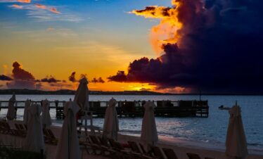 The sun is setting over the beach with umbrellas