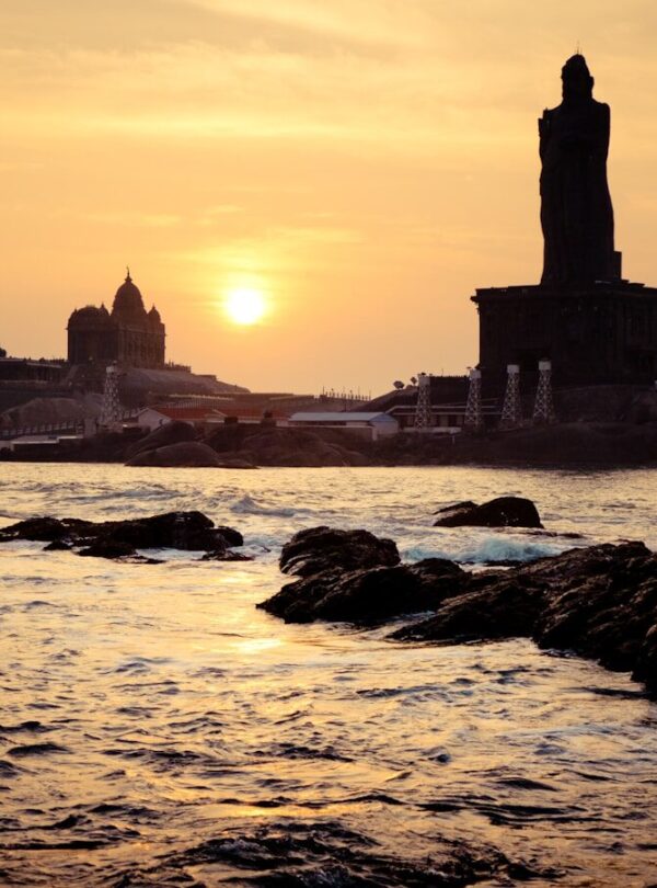 silhouette of building on rock formation near body of water during sunset