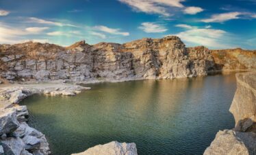 gray rocky mountain beside body of water under blue sky during daytime