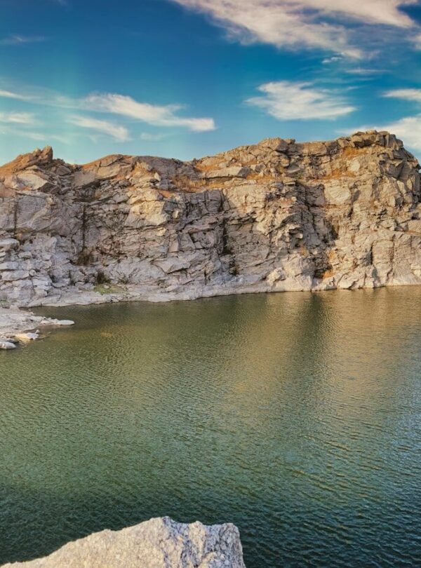 gray rocky mountain beside body of water under blue sky during daytime